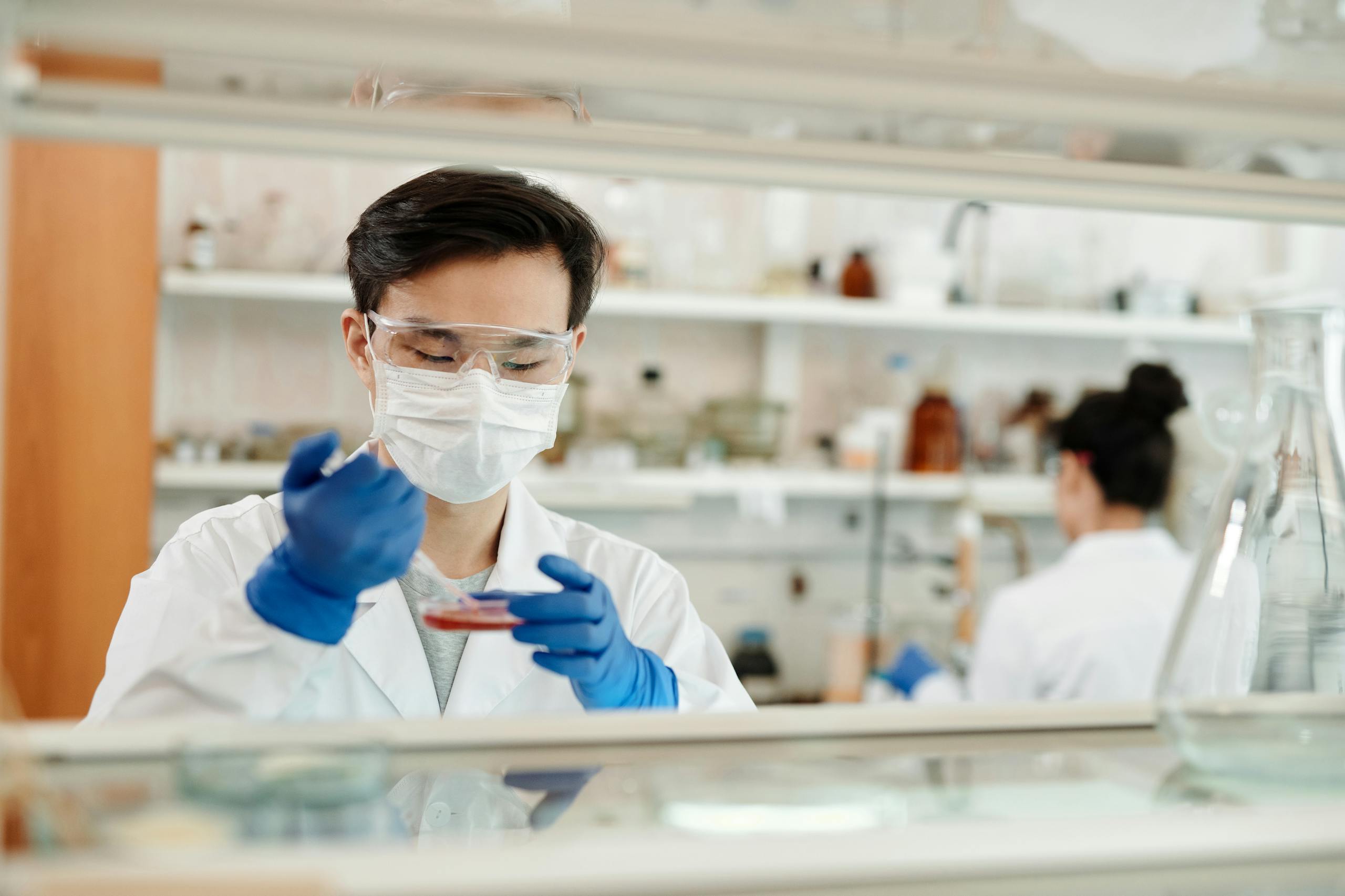 Researcher in a lab coat working on a scientific experiment with a petri dish and protective gear.