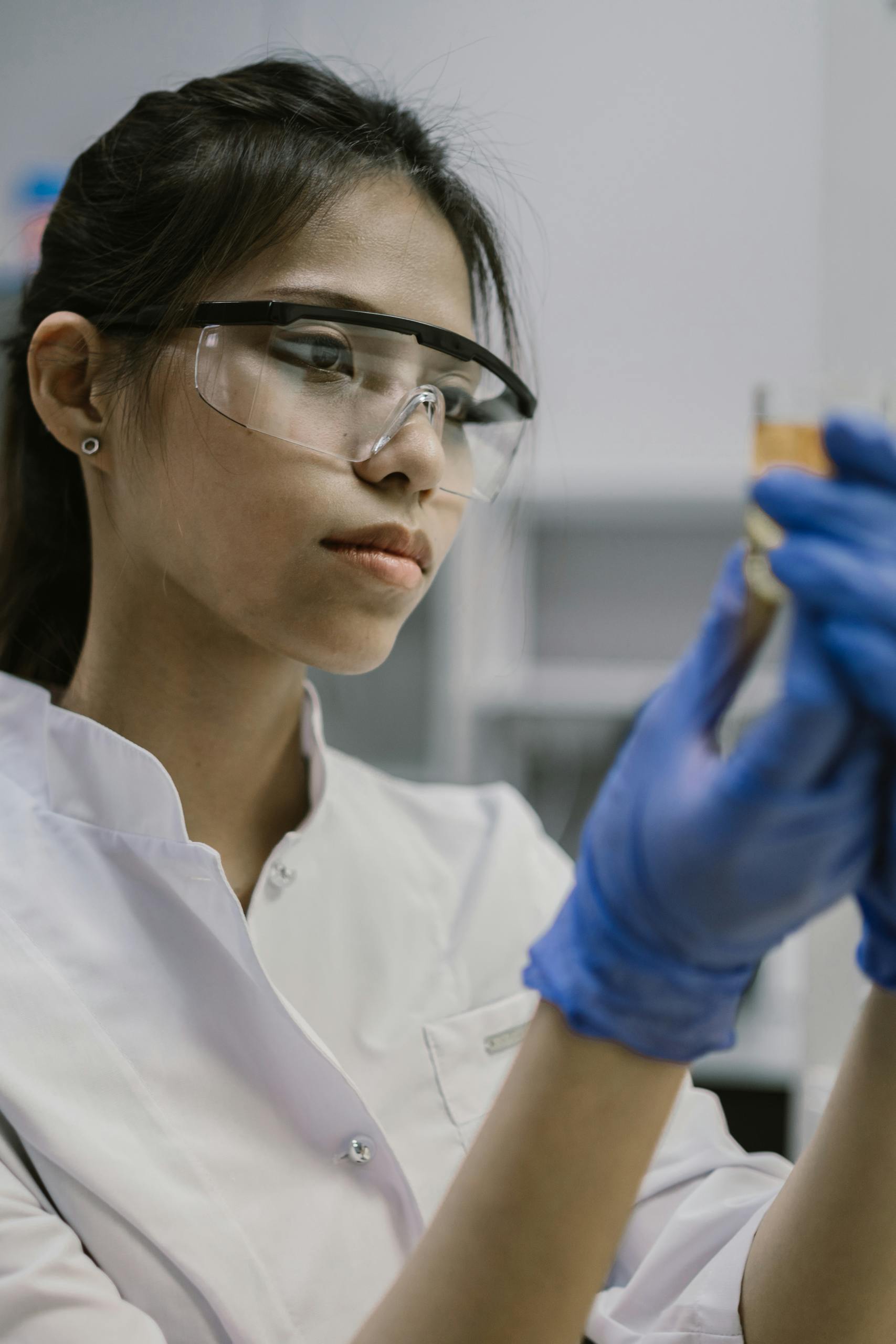 Young female scientist in lab coat and safety glasses conducting an experiment.