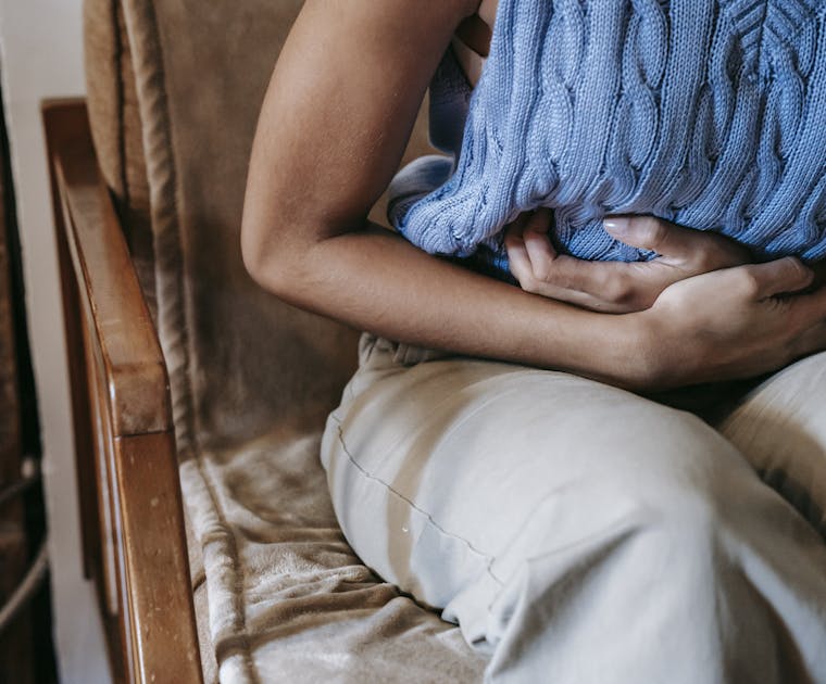 Crop unrecognizable female touching belly while having acute pain in stomach sitting on couch