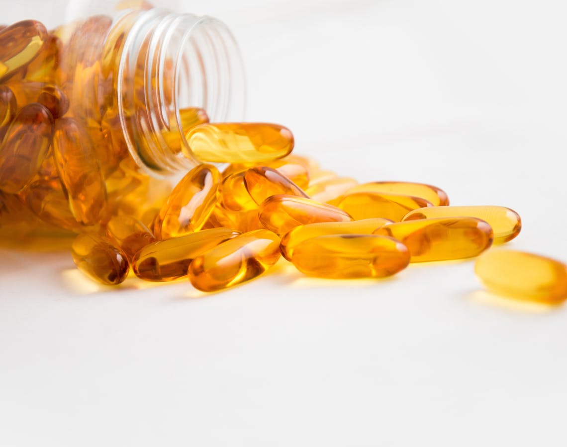 Close-up of fish oil capsules spilling from a bottle on white background.